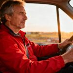 Homme d'âge mûr conduisant un véhicule de transport avec une veste rouge vive, intérieur de voiture moderne