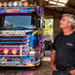 Chauffeur de 50 ans devant son camion Scania personnalisé avec chromes et LEDs dans un atelier