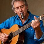 Musicien de 55 ans en chemise bleue jouant de la guitare acoustique avec un bottleneck en studio