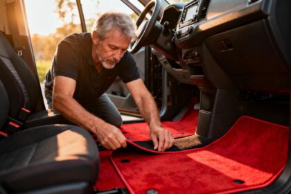 Homme de 55 ans installant des tapis de sol rouges dans l'habitacle sombre d'une voiture
