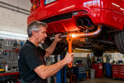 Mécanicien professionnel installant un pot d'échappement rouge vif sur une voiture de sport dans un garage équipé