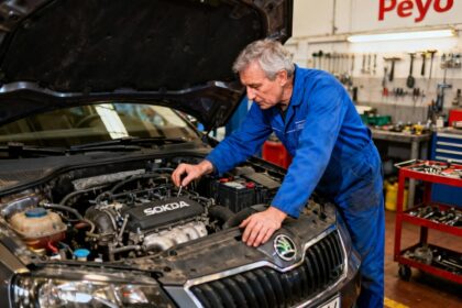 Mécanicien en bleu de travail inspectant le moteur d'une Skoda dans l'atelier Peyo Automobiles