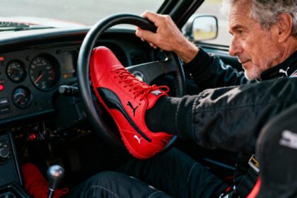 Pilote de 50 ans concentré au volant, portant des chaussures de course Puma Speedcat rouges dans un cockpit authentique