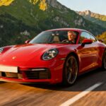 Porsche 911 Carrera T rouge en conduite sur une route de montagne près d’Annecy, paysage verdoyant en arrière-plan