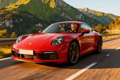 Porsche 911 Carrera T rouge en conduite sur une route de montagne près d’Annecy, paysage verdoyant en arrière-plan