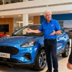 Vendeur professionnel de 55 ans en chemise bleue montre une Ford Puma Gen-E électrique dans un showroom moderne